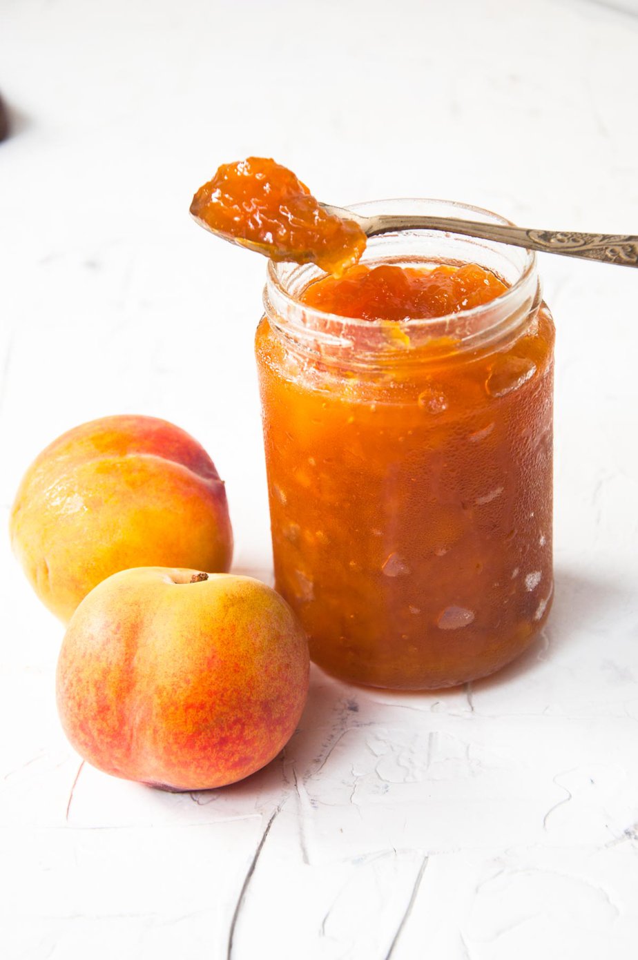 Peach jam jar with two fresh peaches on the left. 