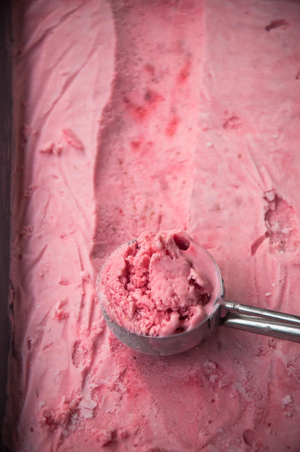 Strawberry ice cream in a with scoop  on it, ready to serve.