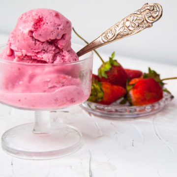Two ice cream scoops in a cup with strawberries in the background.