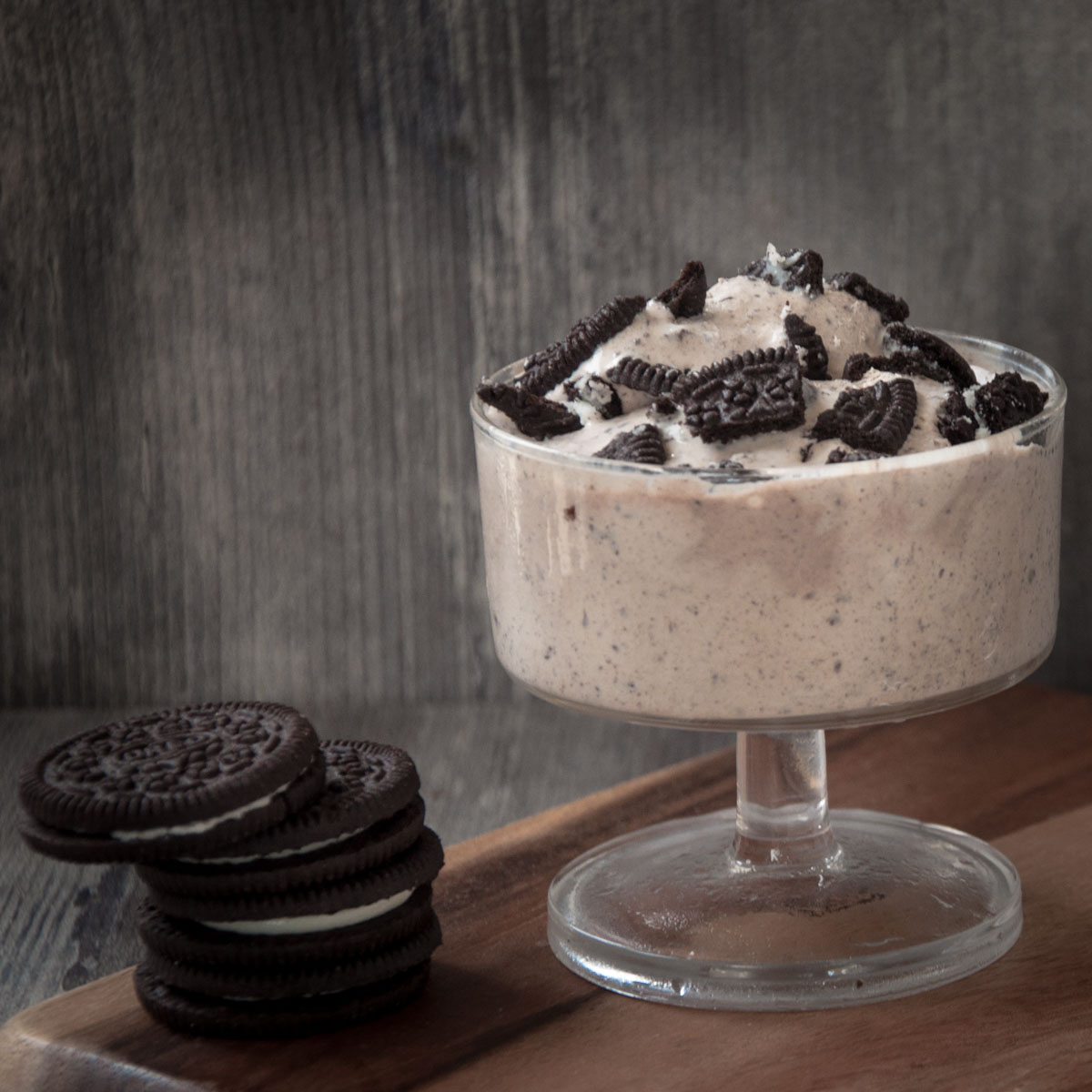 Oreo ice cream served in a glass cup with oreo cookies stacked in foreground.
