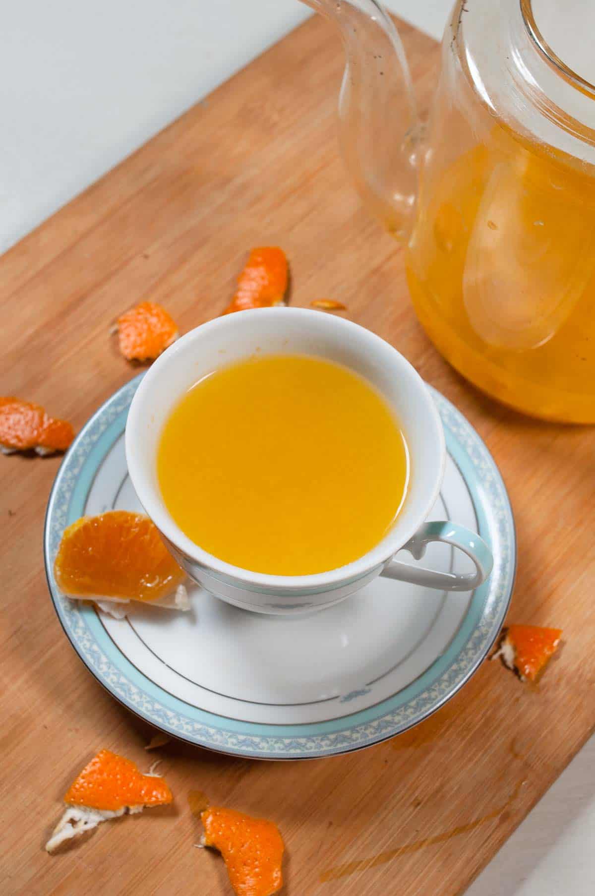 A cup of orange with orange peel around it and a kettle with tea in the background.