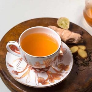 A cup of ginger green tea with ginger and lemon in the background.
