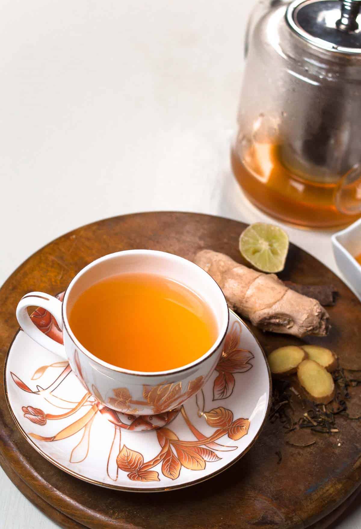 Ginger green tea served in a cup with a glass kettle in the background.