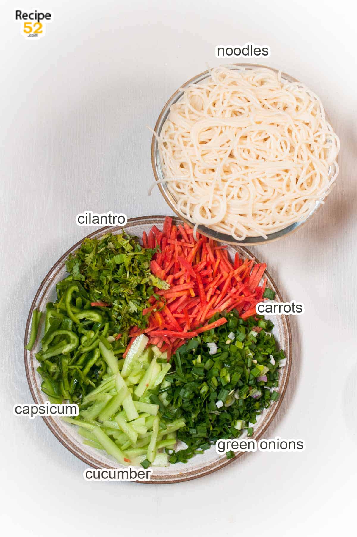Noodles in a bowl and assorted veggies in a plate on the white background.