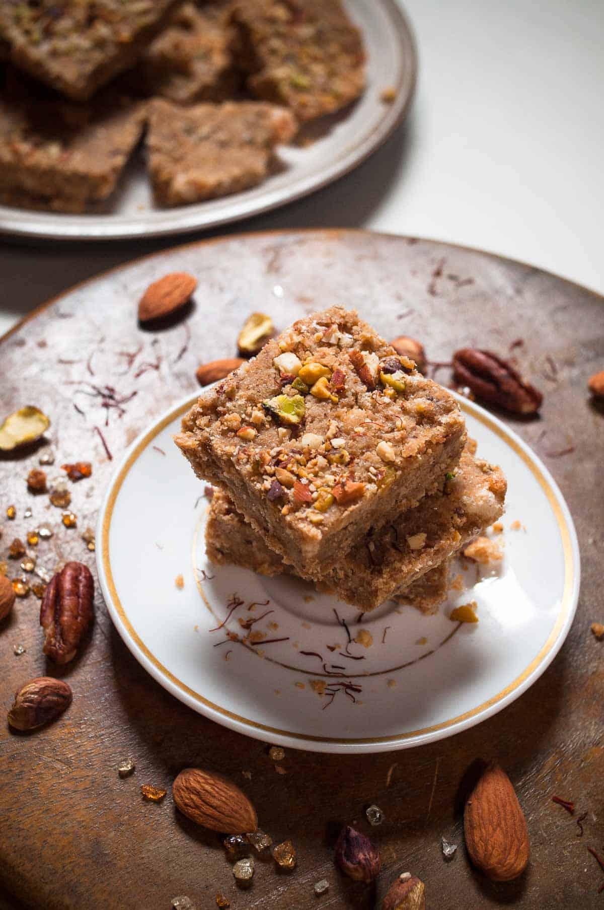 Gol papdi squares stacked on a white plate with nuts scattered in the background.