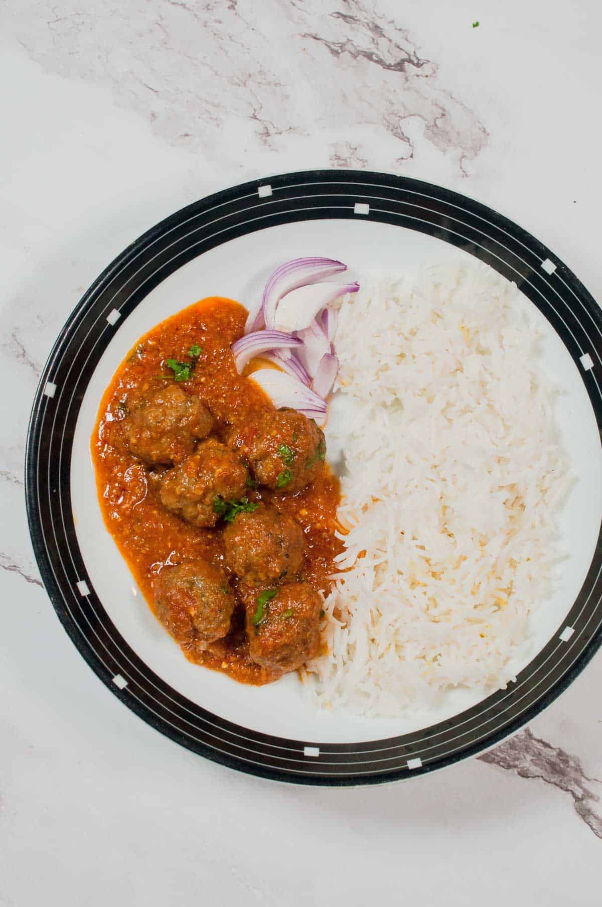 Kofta curry served in the with white rice on the white marble background.
