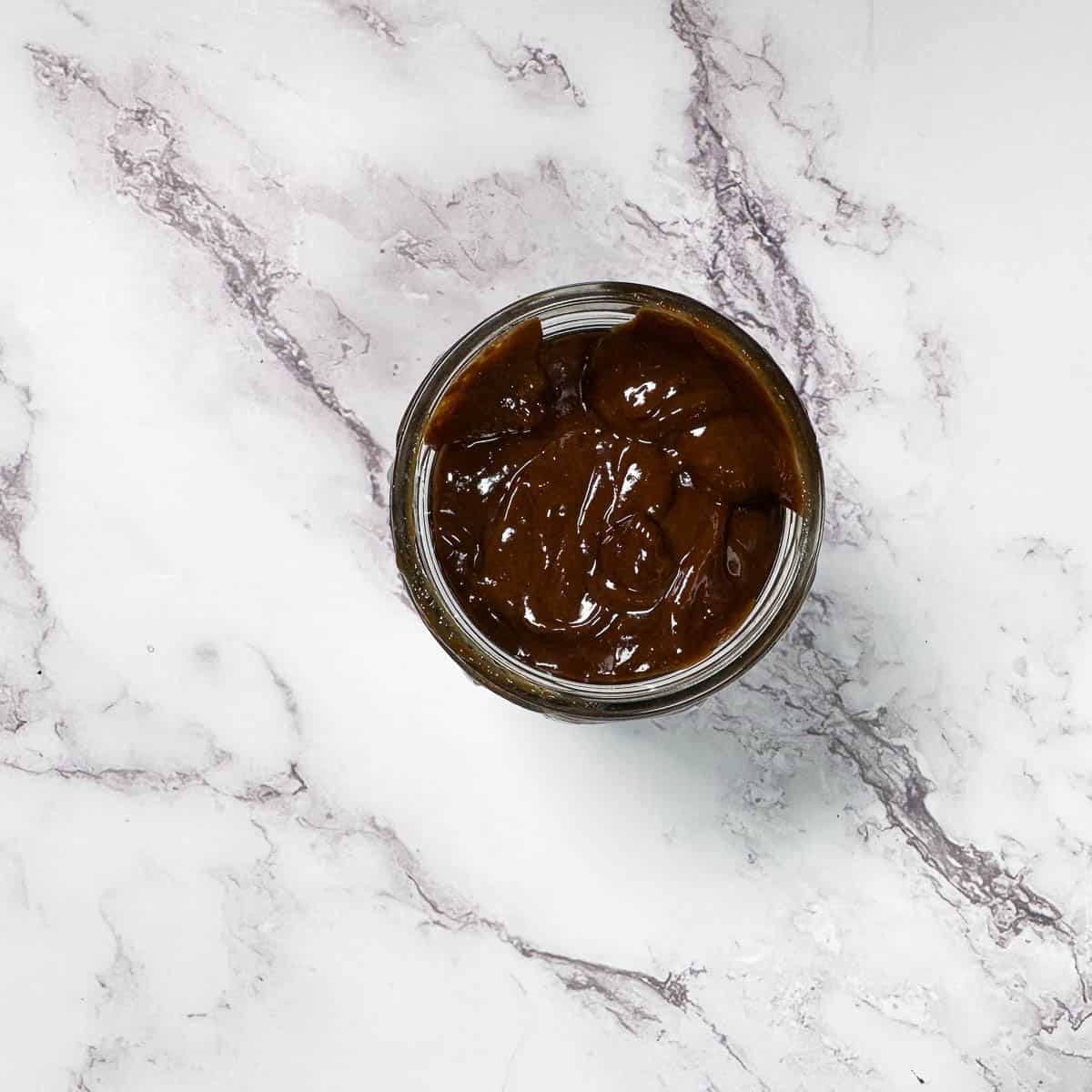 Hoisin sauce in jar on the white marble background.