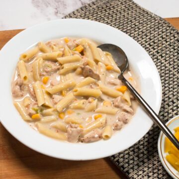 Chicken Pasta with white sauce served in a white ceramic plate with a metallic spoon.