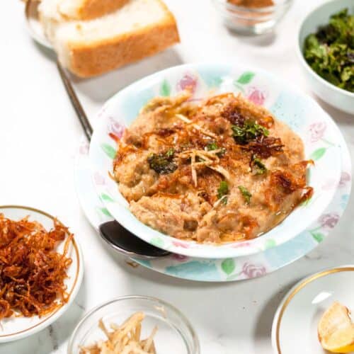 Haleem served in a bowl with fried onion, lemon and bread in the background.