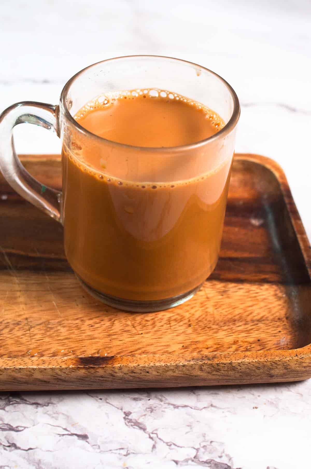 A cup of karak chai placed on a wooden tray.