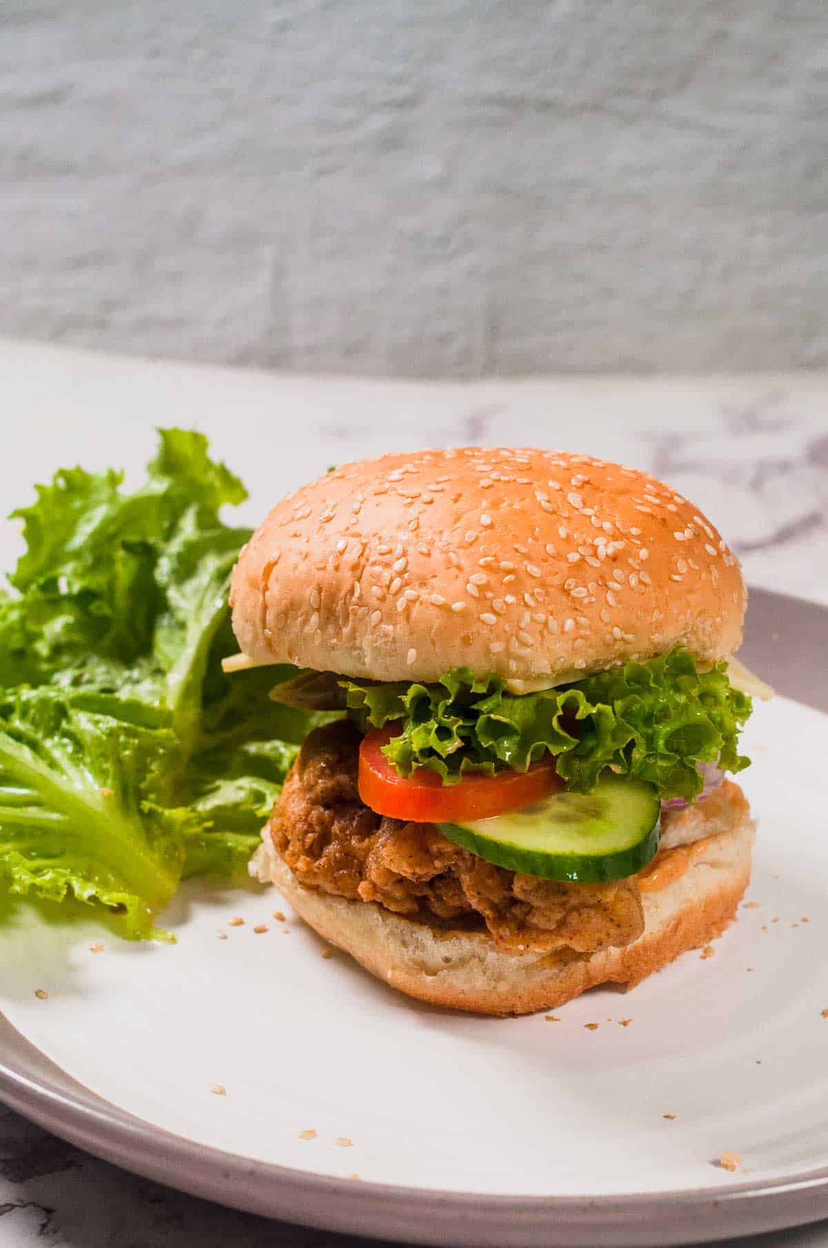 Spicy chicken sandwich served in a plate with fresh lettuce leaves.