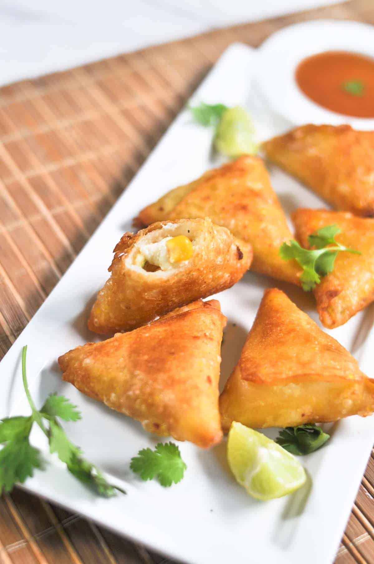 Cheese samosa served in a white platter garnished with cilantro and with a red sauce.