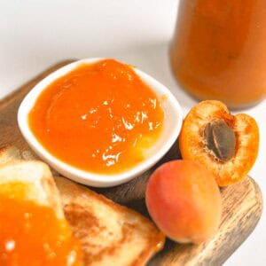 Apricot jam served in a plate on wooden cutting board.