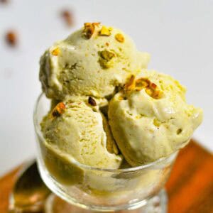 Scoops of nutty ice cream in a bowl with pistachios on top.