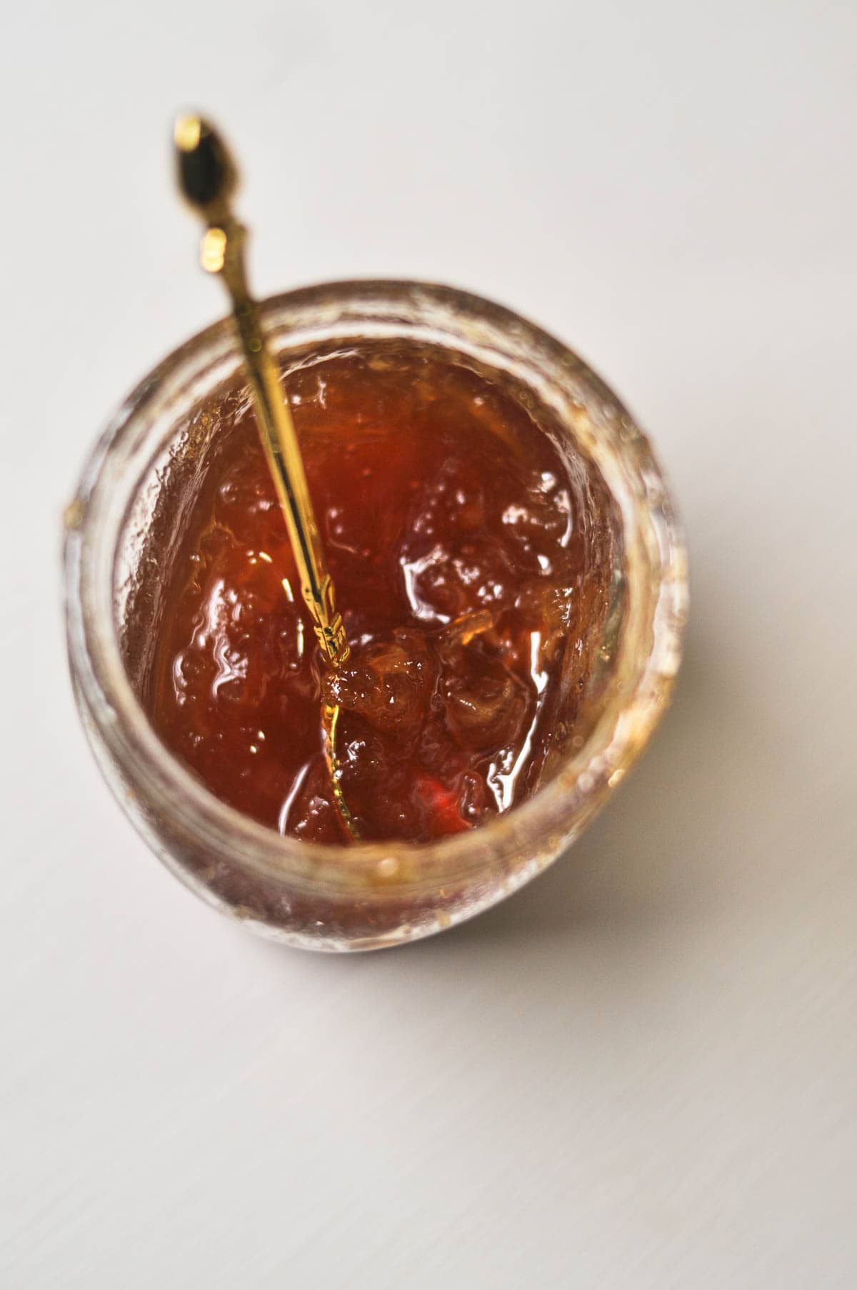 Lemon marmalade in a glass jar with a golden spoon inside.