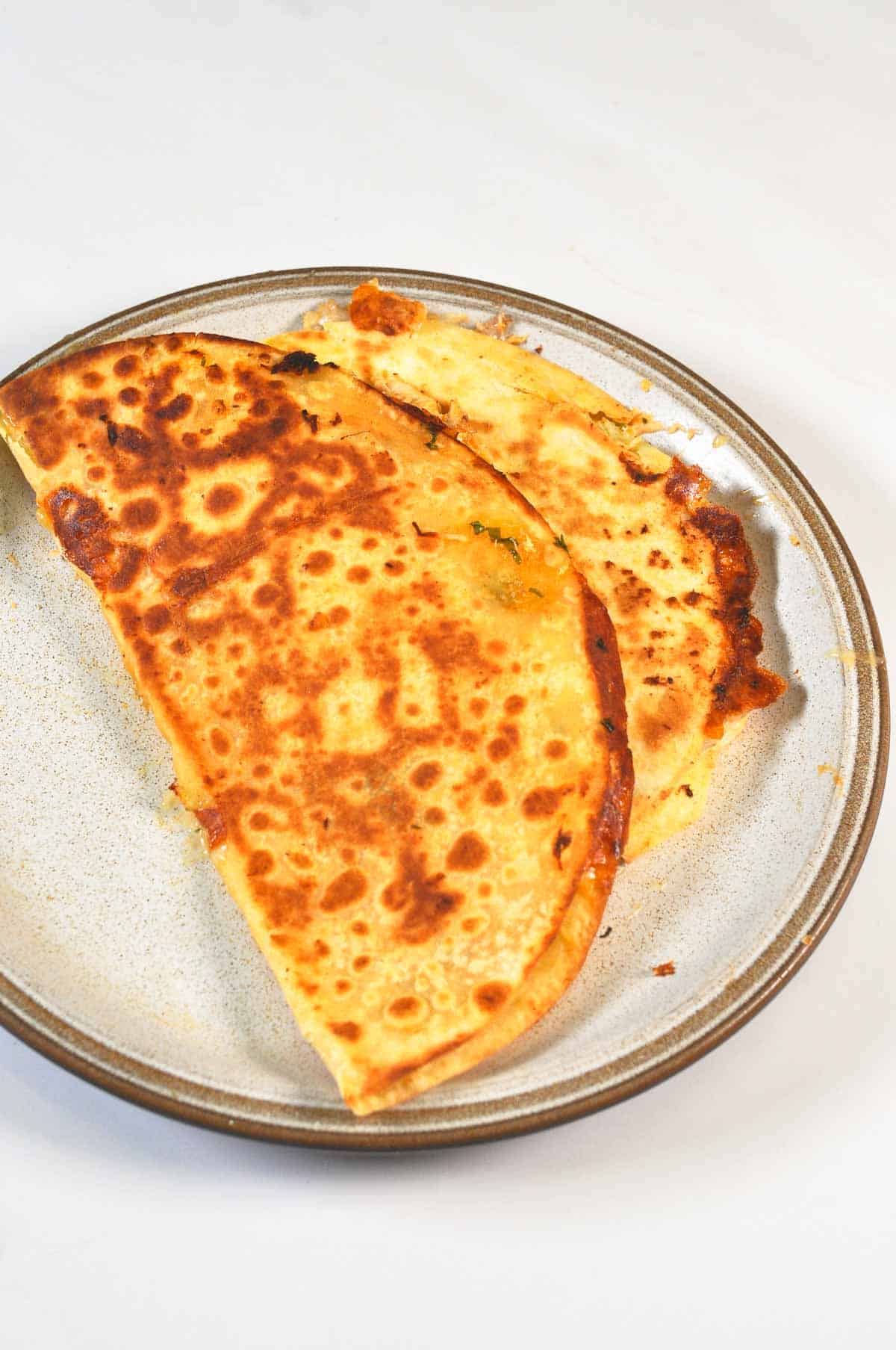 Two toasted half mooned shaped quesadilla served on a plate.