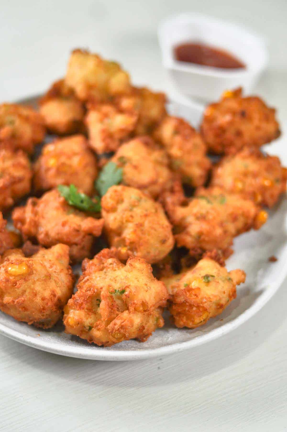 A platter of corn fritters served with tomato sauce.