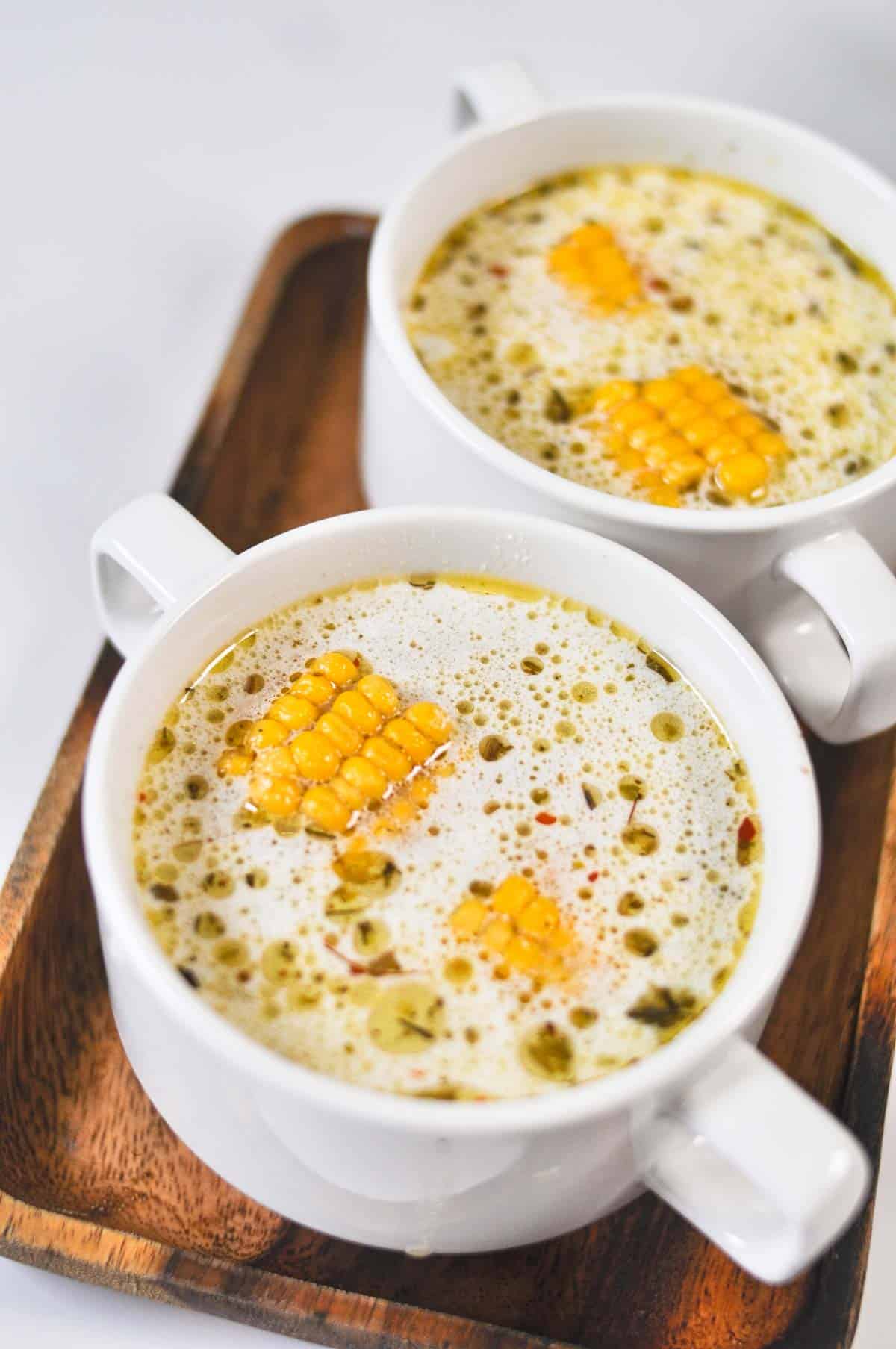 Two ceramic bowls filled with soup with corn cobs in them.
