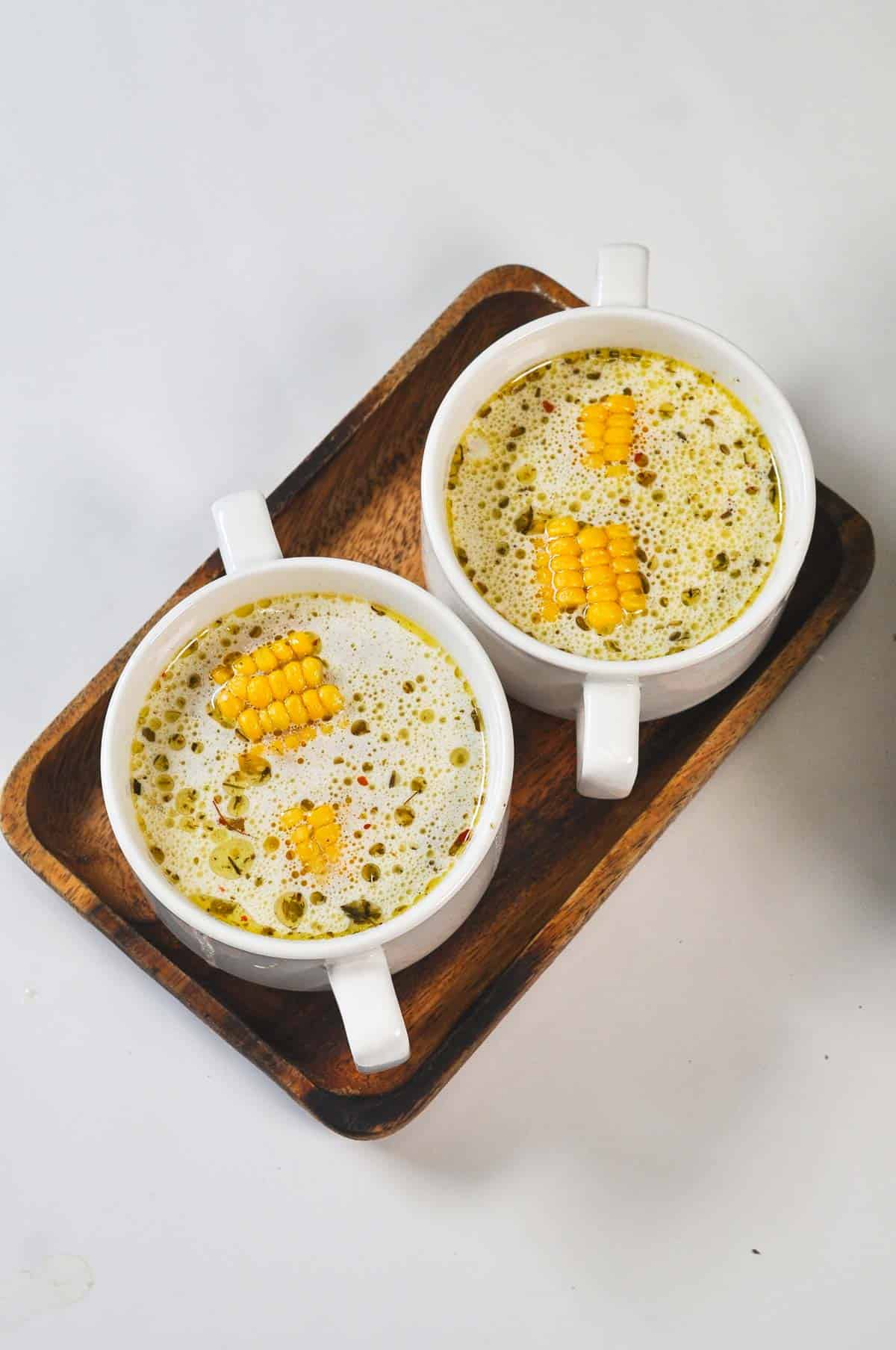 Two bowls of soup served on wooden tray.