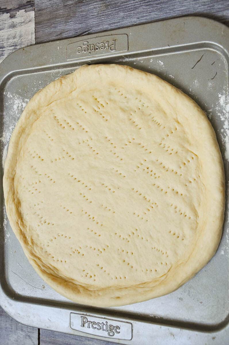 Pizza dough rolled out on a baking tray.
