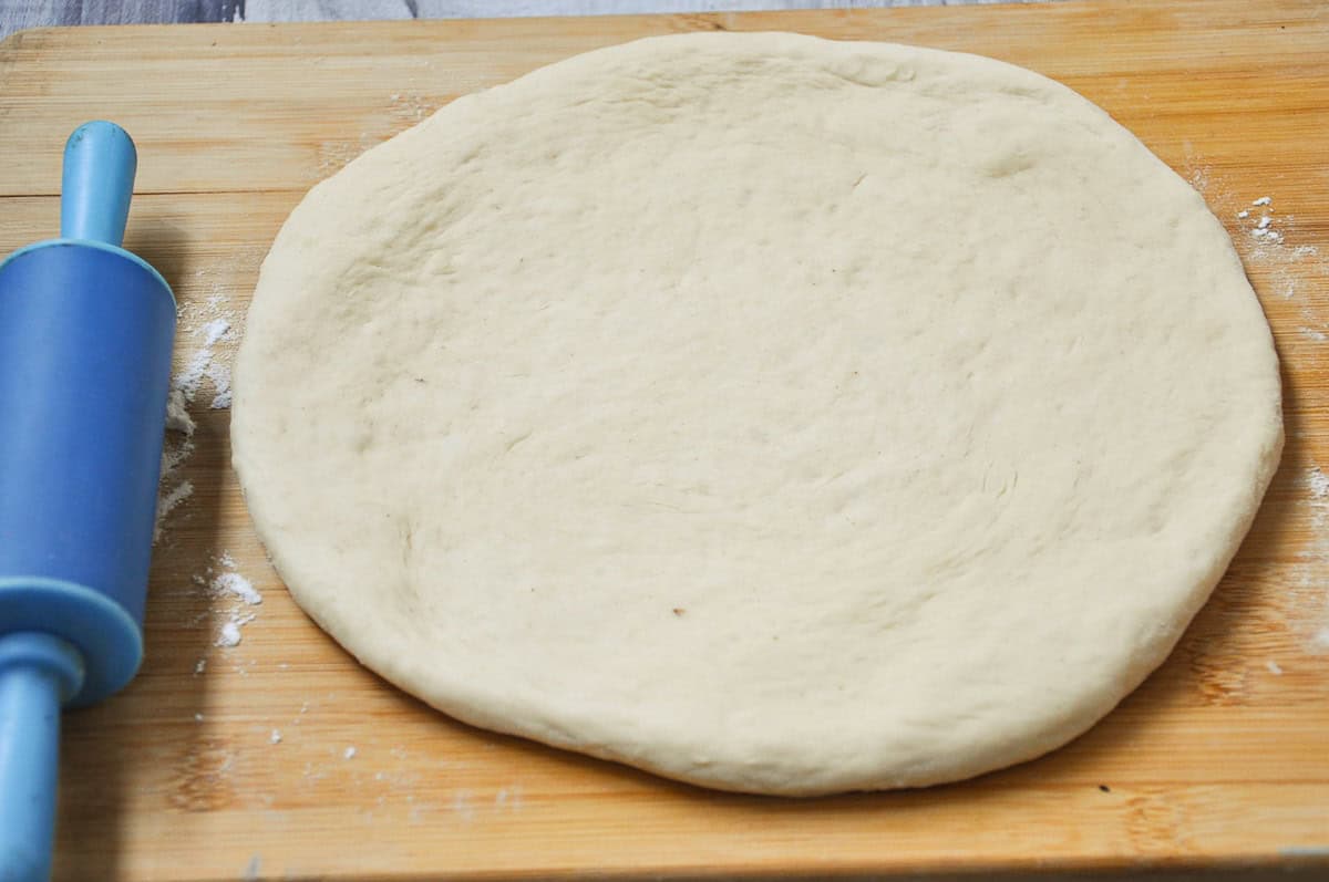 The pizza dough is on a wooden table next to a rolling pin.